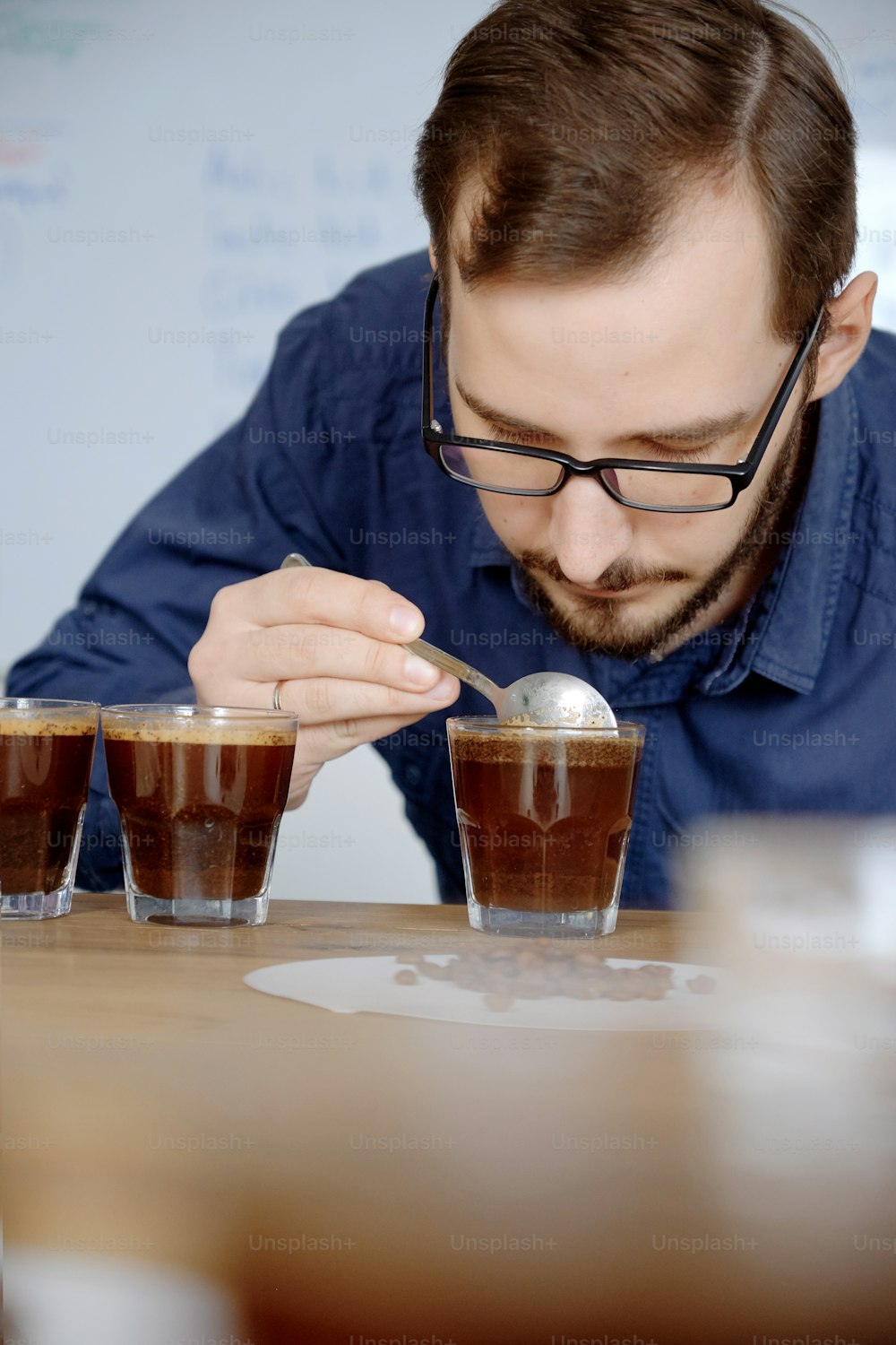 Retrato do homem cheirando café recém-fabricado em copo de vidro, usando colher, examinando o sabor e o sabor do café no teste de xícara de café para barosta