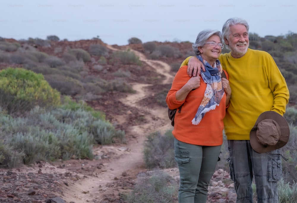 해질녘에 야외 여행에서 껴안고 있는 웃는 노부부. 산과 자연을 즐기는 은퇴자들을 위한 건강한 라이프스타일