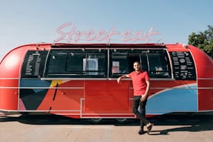 Happy young clerk in uniform standing by street food truck in urban environment