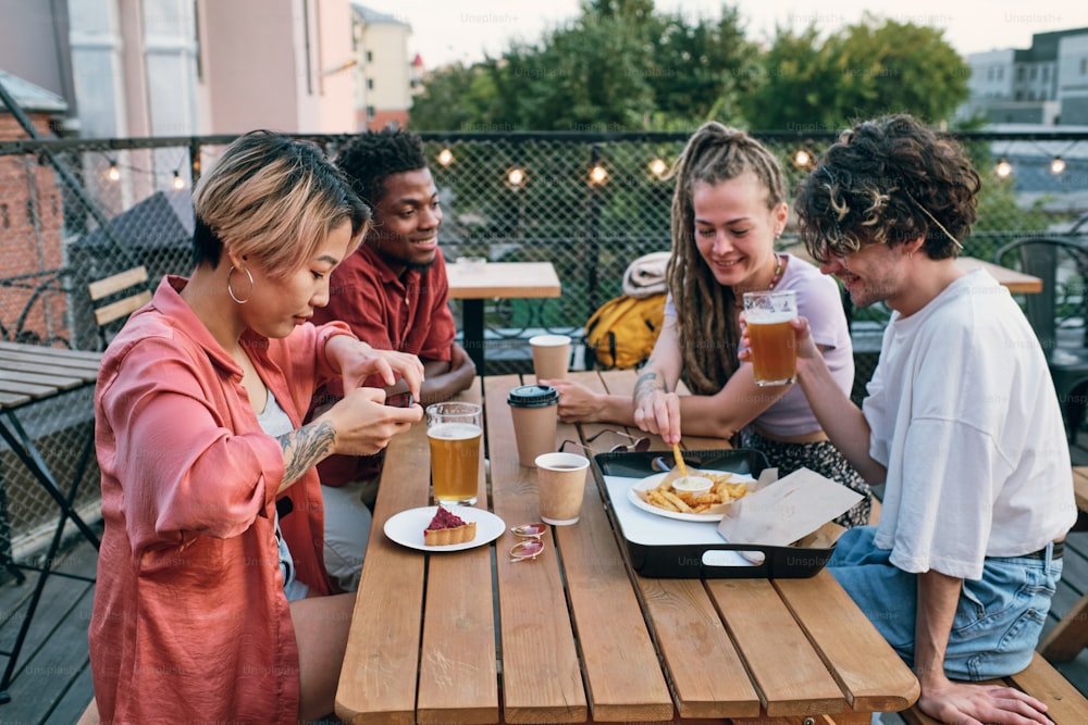 Jovens amigos interculturais felizes tendo fast food e bebidas à mesa no café ao ar livre