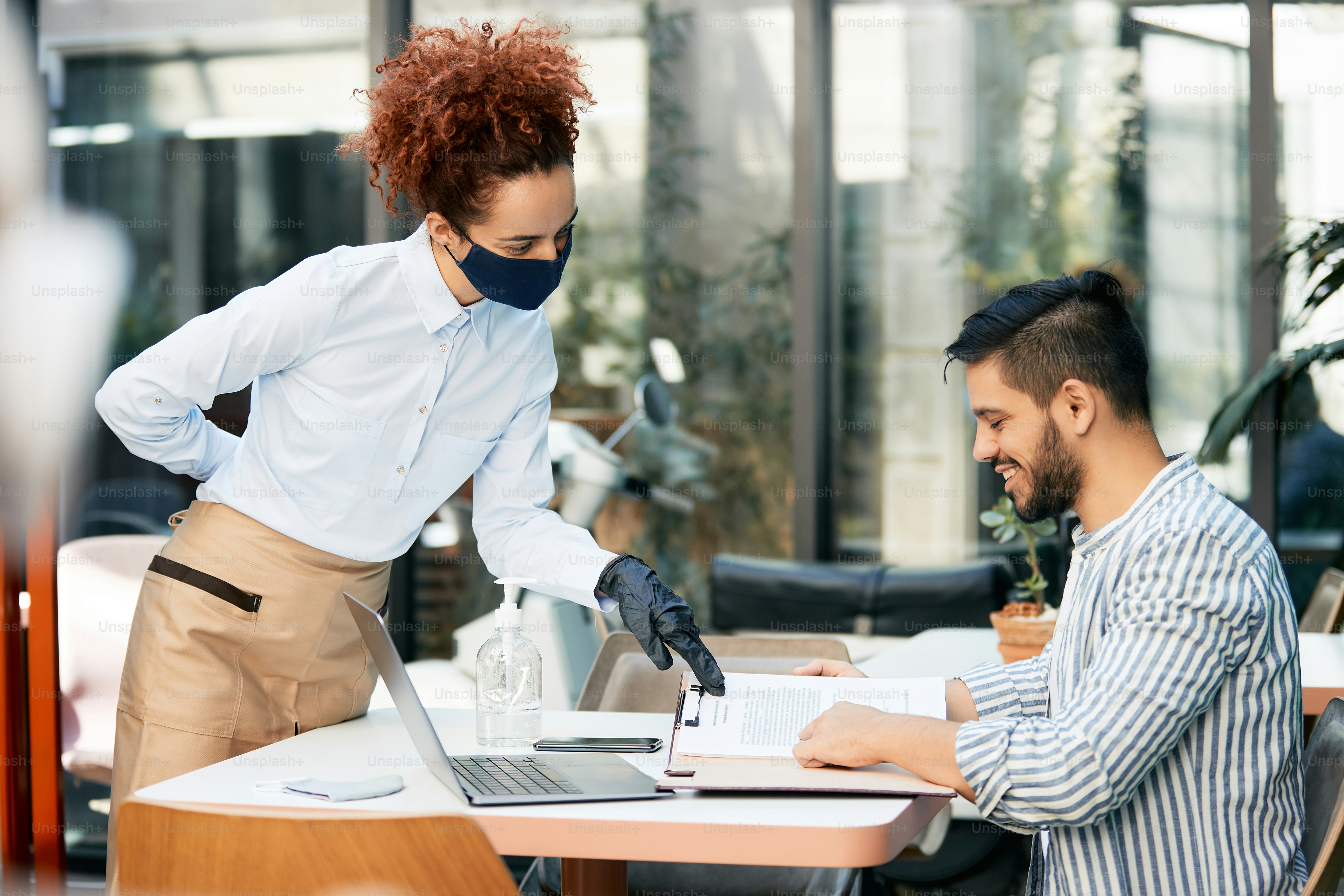 Waitress wearing face mask while showing menu to a guest in a cafe.