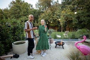 Multiracial couple hanging out together during a dinner at their backyard in the evening. Standing with drinks. Concept of relationship. Black man and european woman enjoying time together