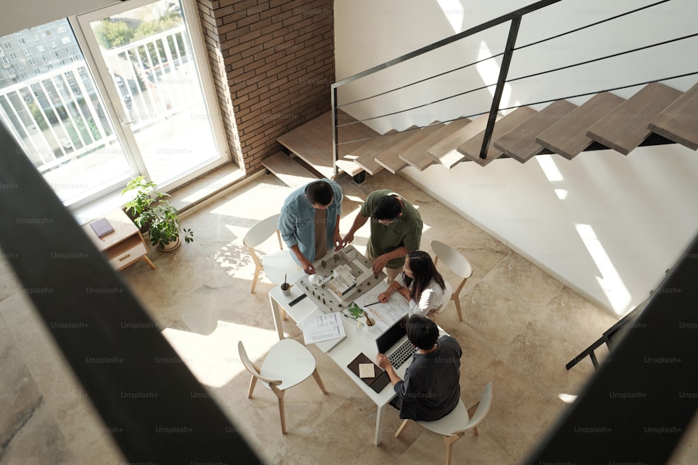 4명의 젊은 중국 건축가가 대형 사무실에서 테이블 옆에 서서 신도시 지구의 배치에 대해 논의하고 있다