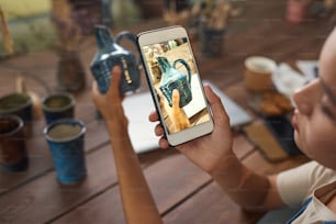 スマートフォンの画面に焦点を合わせる:ワークショップで陶器の花瓶の写真を撮る陶芸家