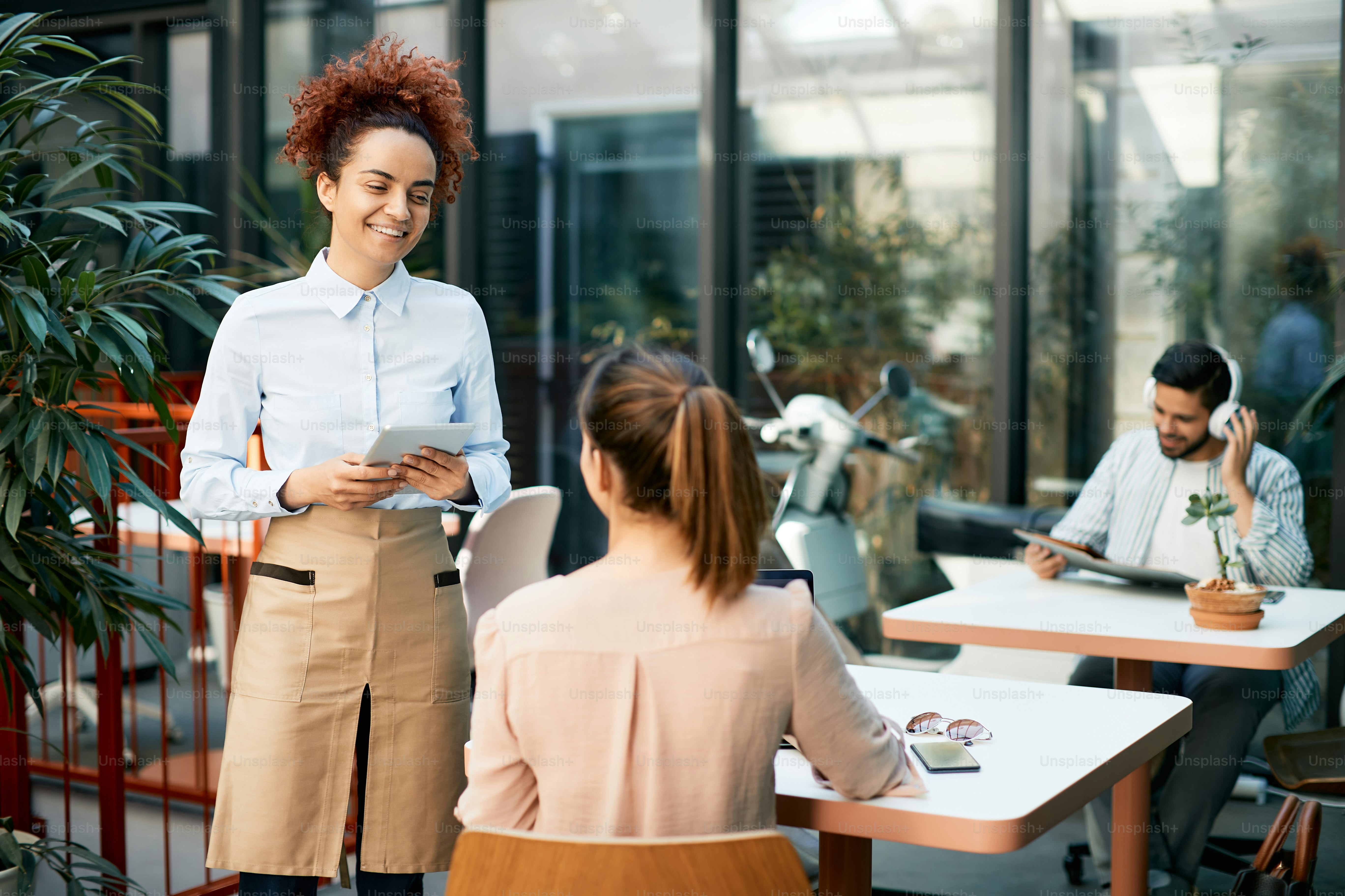 Young waitress using touchpad while taking order from female customer in a cafe.