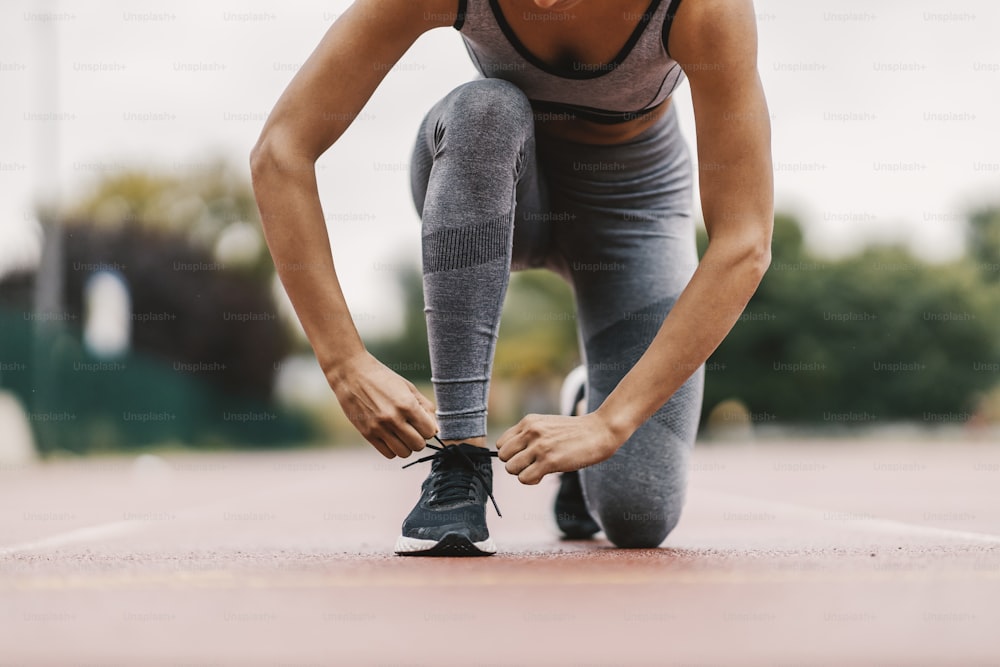 Cut out picture of a sportswoman kneeling in the stadium and tying a shoelace on her sneaker. A woman is preparing for a long run in the stadium. Sportswoman tying shoelace.