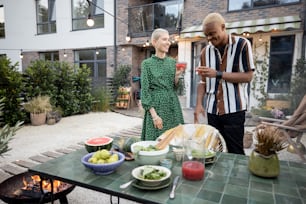 Multiracial couple hanging out together during a dinner at their backyard in the evening. Clinking glasses and having fun. Concept of relationship. Black man and european woman enjoying time together