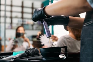 Close-up of hairstylist squeezing hair color from tube while working in a salon.