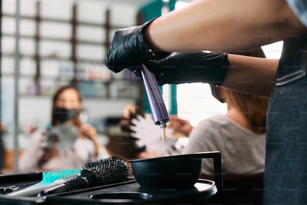 Close-up do cabeleireiro espremendo a cor do cabelo do tubo enquanto trabalha em um salão.