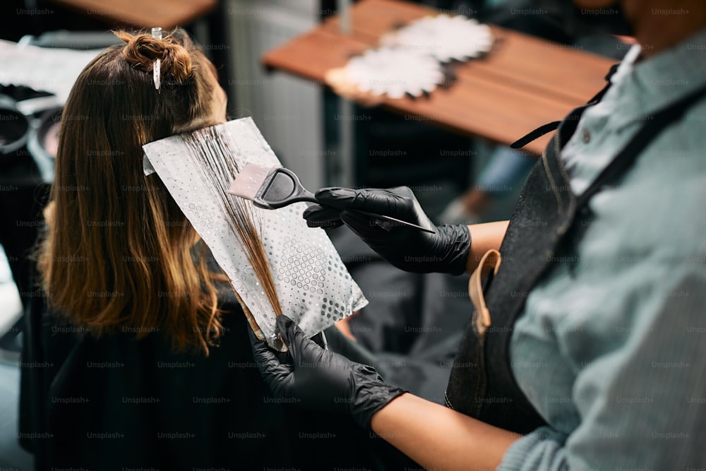 Primo piano del parrucchiere che applica la tintura sui capelli della donna in un salone.