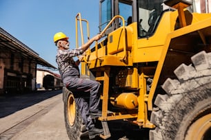 A senior heavy industry worker is climbing the bulldozer and getting ready to drive it. A driver climbing the bulldozer.