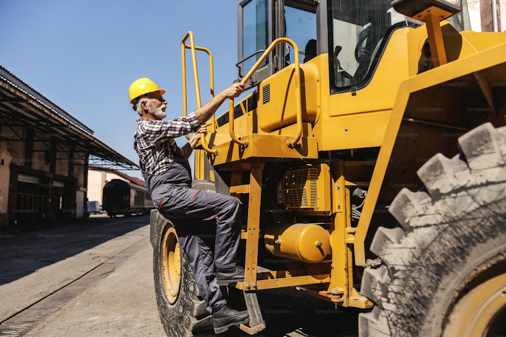Un trabajador de la industria pesada de alto rango se sube a la excavadora y se prepara para conducirla. Un conductor subiendo a la excavadora.