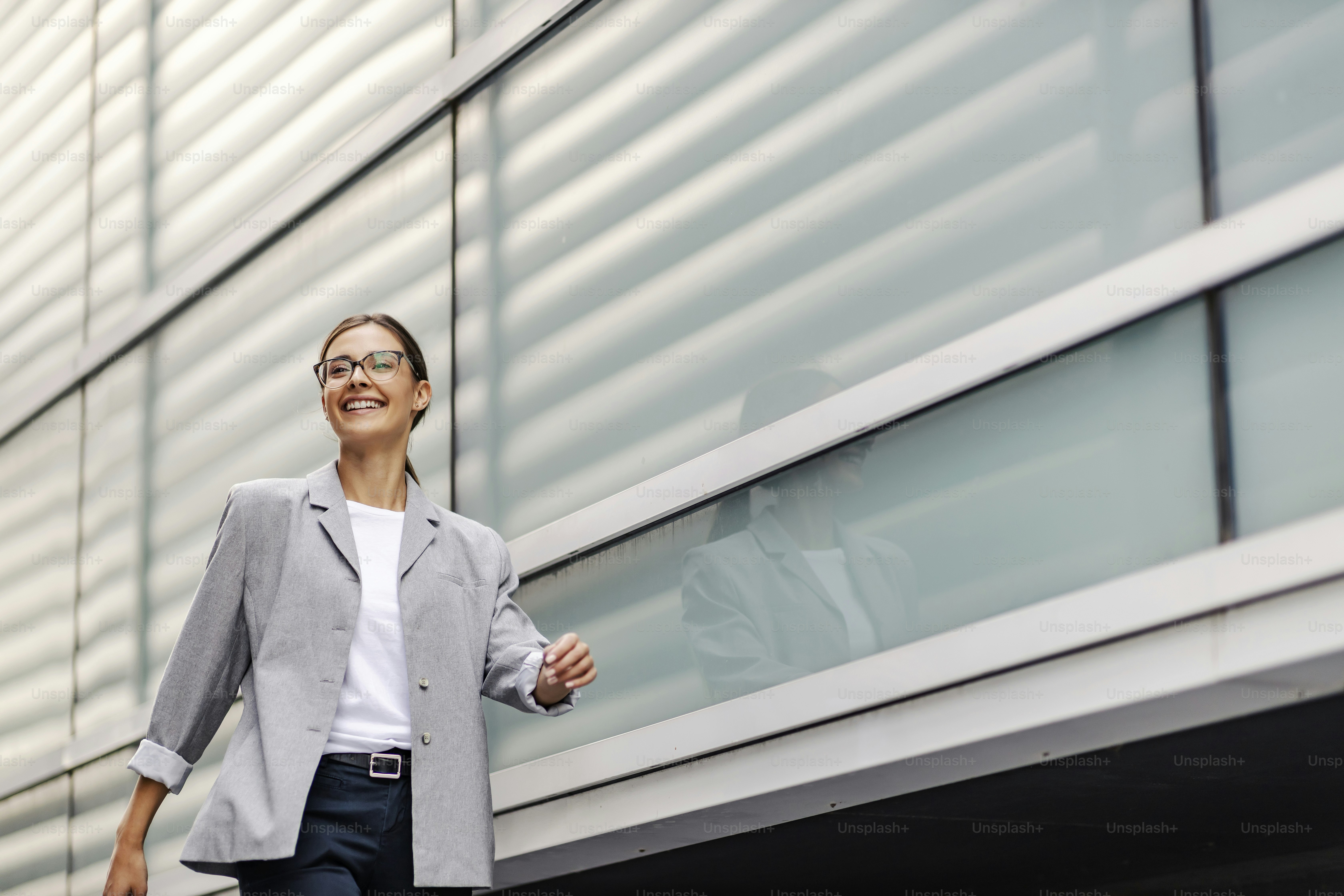 A happy young businesswoman rushing to her office. A businesswoman passing by windows on the business center and going to her workplace. A businesswoman walking outside