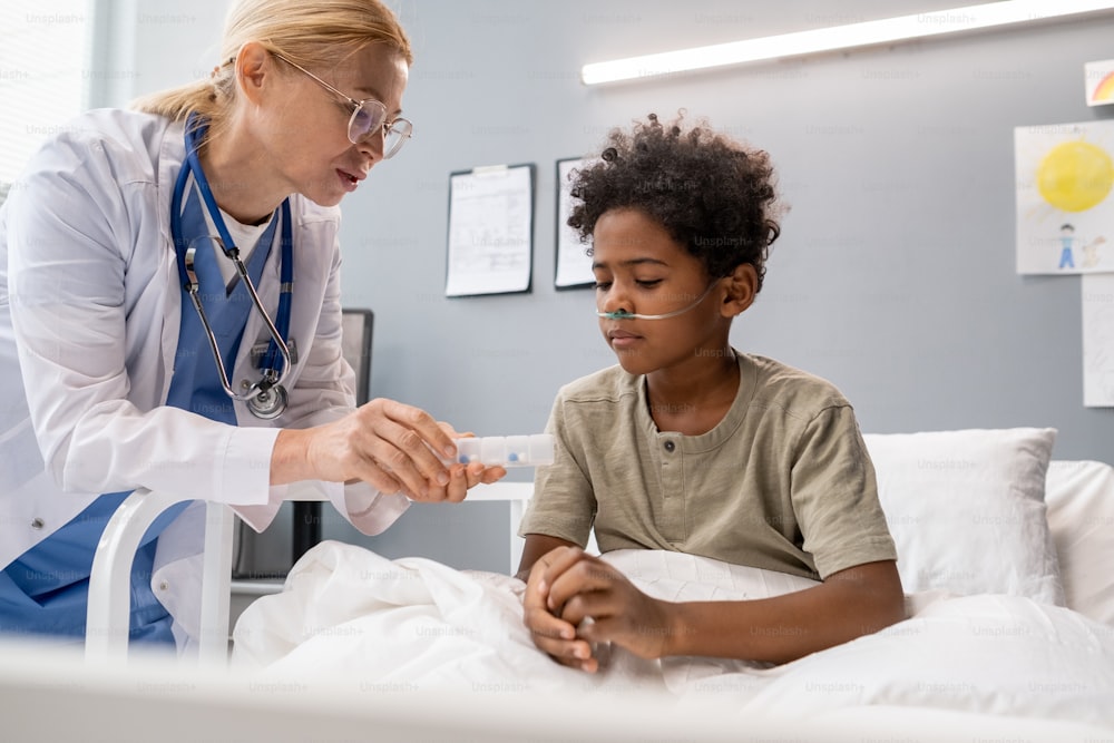 Ärztin macht Infusion für kleinen Jungen, der während seiner Behandlung im Krankenhaus auf dem Bett sitzt