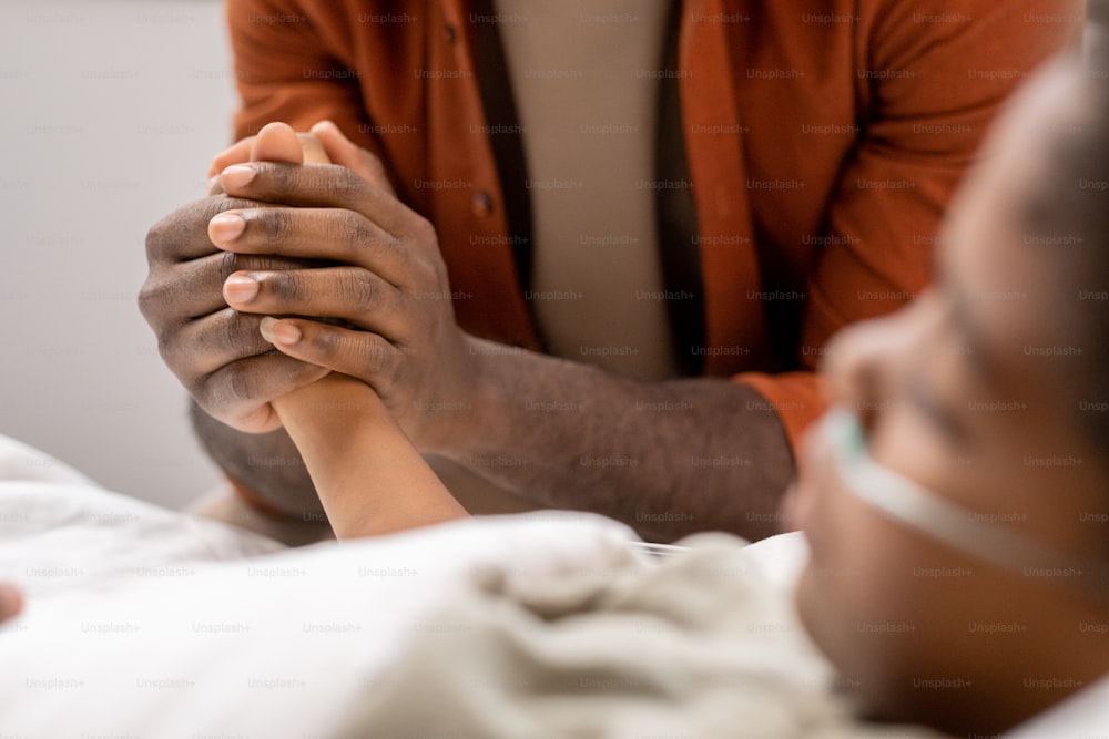 Close-up of loving parent holding hand of his sick child and supporting him while he lying at hospital