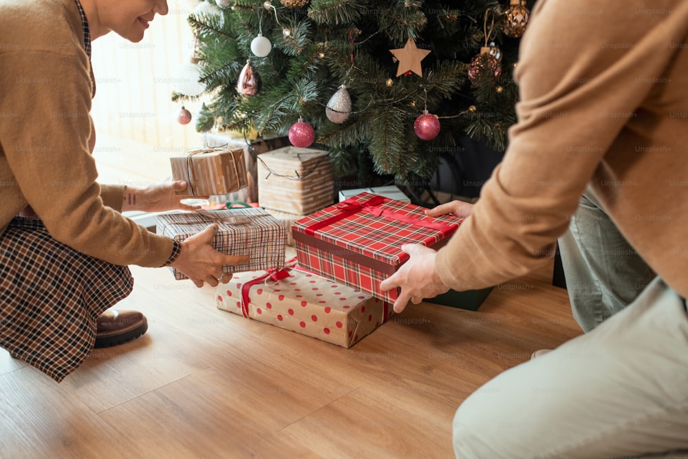 Close-up of couple sitting on floor and stacking Christmas presents under tree