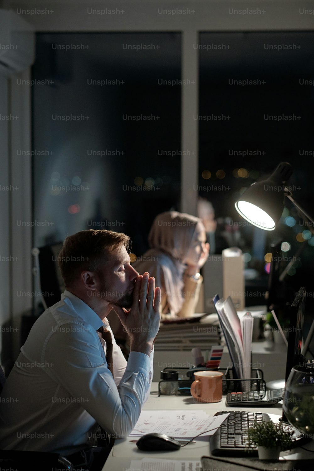 Uomo d'affari stanco con le sue mani messe insieme da faccia seduta davanti al monitor del computer contro la collega femminile