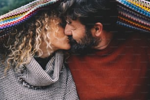 Couple in love kissing under a colorful woolen blanket. Concept of mature people in relationship and life forever. Man kiss woman with romance. Enjoying life with love