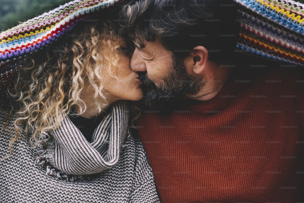 Couple in love kissing under a colorful woolen blanket. Concept of mature people in relationship and life forever. Man kiss woman with romance. Enjoying life with love