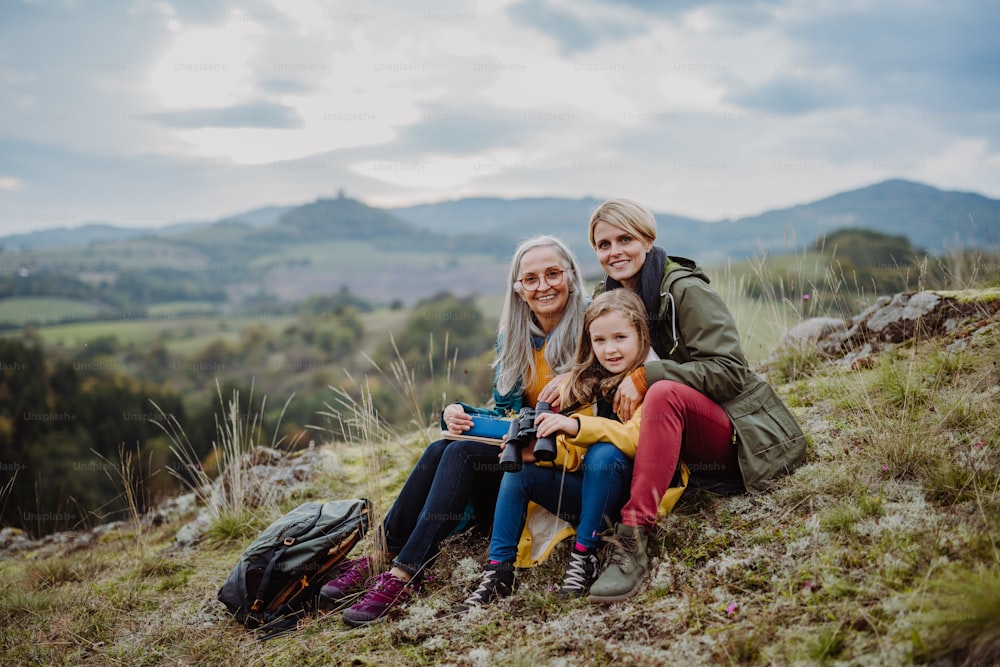 A small girl with mother and grandmother sitting and lookiong at camera on top of mountain.