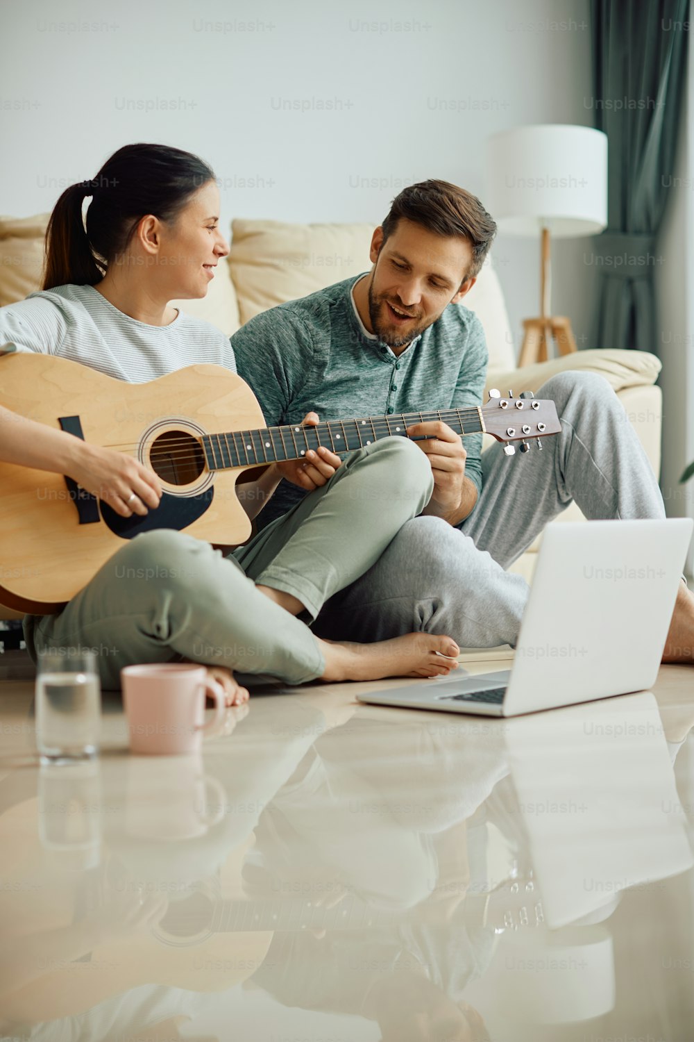 Happy woman learning to play acoustic guitar with help of her husband at home. Copy space.