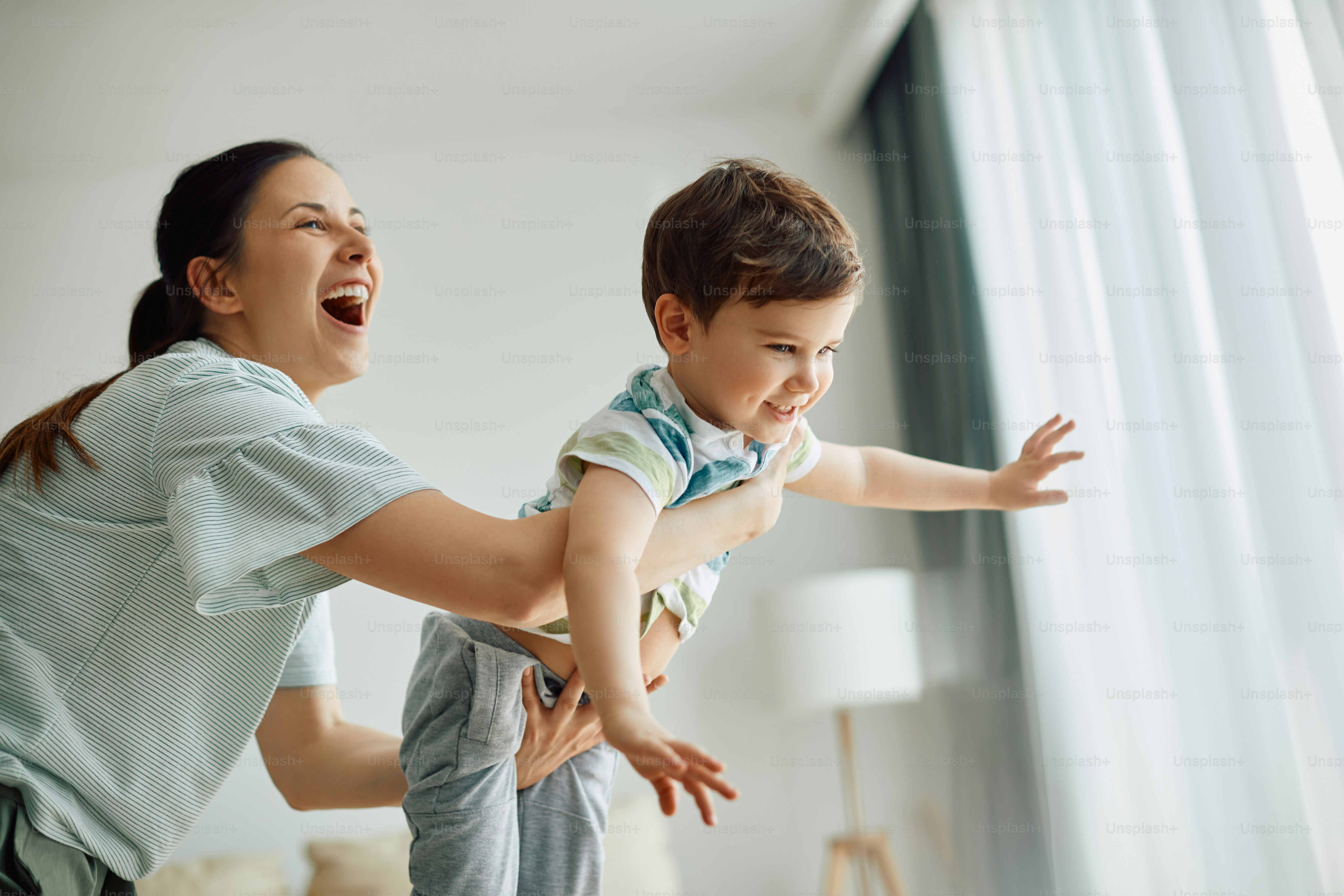 Cute happy boy having fun with his playful mother at home and looking ...