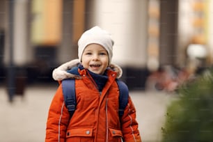 Happy kindergarten child with a backpack outdoors. A happy cute little kindergarten boy standing outdoors with a backpack on his back and going to kindergarten.