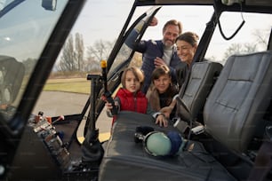 Excited parents and children peeking into a cockpit of a helicopter while preparing to fly