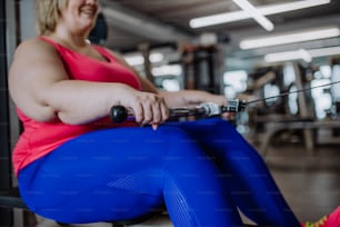 Eine nicht wiederzuerkennende Plus-Size-Frau, die drinnen im Fitnessstudio auf einem Rudergerät trainiert
