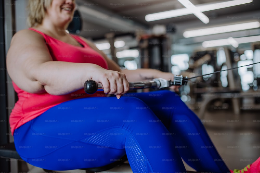 An unrecognizable plus size woman training on rowing machine machine indoors in gym