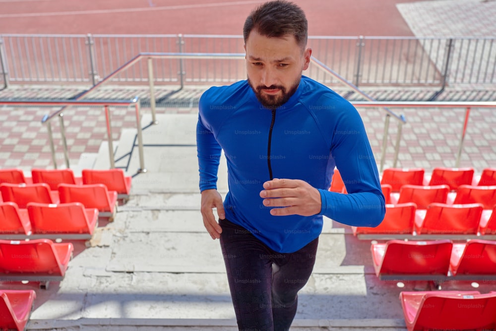 Porträt eines Mannes mittleren Alters mit Bart, der die Treppe im Stadion hinaufjoggt, er rennt vorwärts