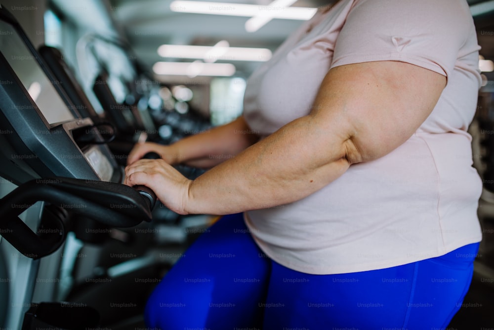 A midsection of overweight woman exercising on treadmill indoors in gym
