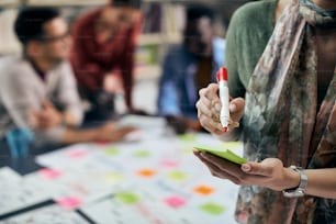 Close-up of creative woman writing on sticky note during business meeting at casual office.