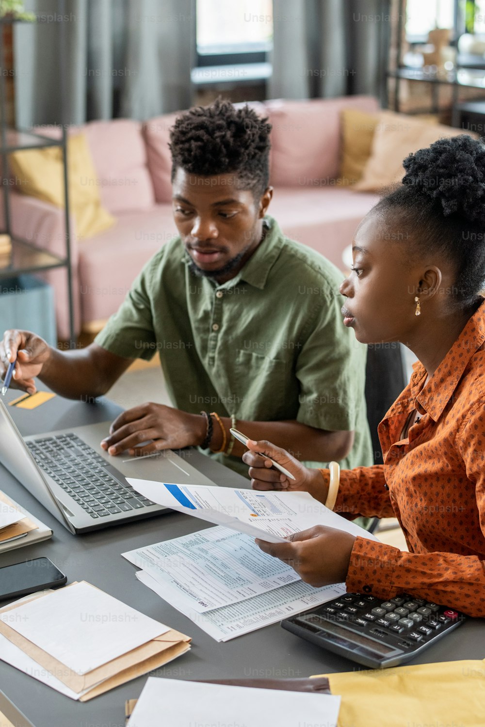 Ernsthaftes junges afroamerikanisches Paar sitzt am Tisch und gibt Rechnungsdaten ein, während es das Steuerformular online ausfüllt