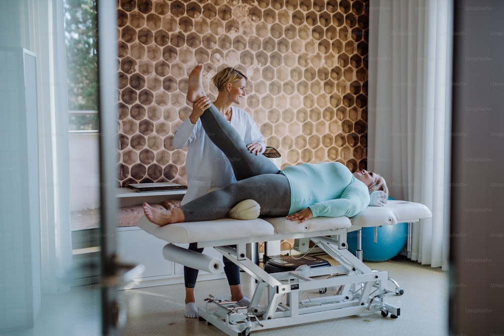 Une femme kinésithérapeute adulte moyenne faisant de l’exercice avec une femme en surpoids à l’intérieur dans un centre de rééducation