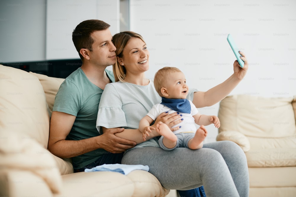 Young happy parents taking selfie with their baby son at home.