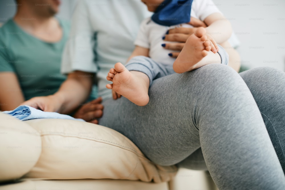 自宅のソファでくつろぐ両親と赤ん坊の息子の接写。男の子の足に焦点が当てられています。