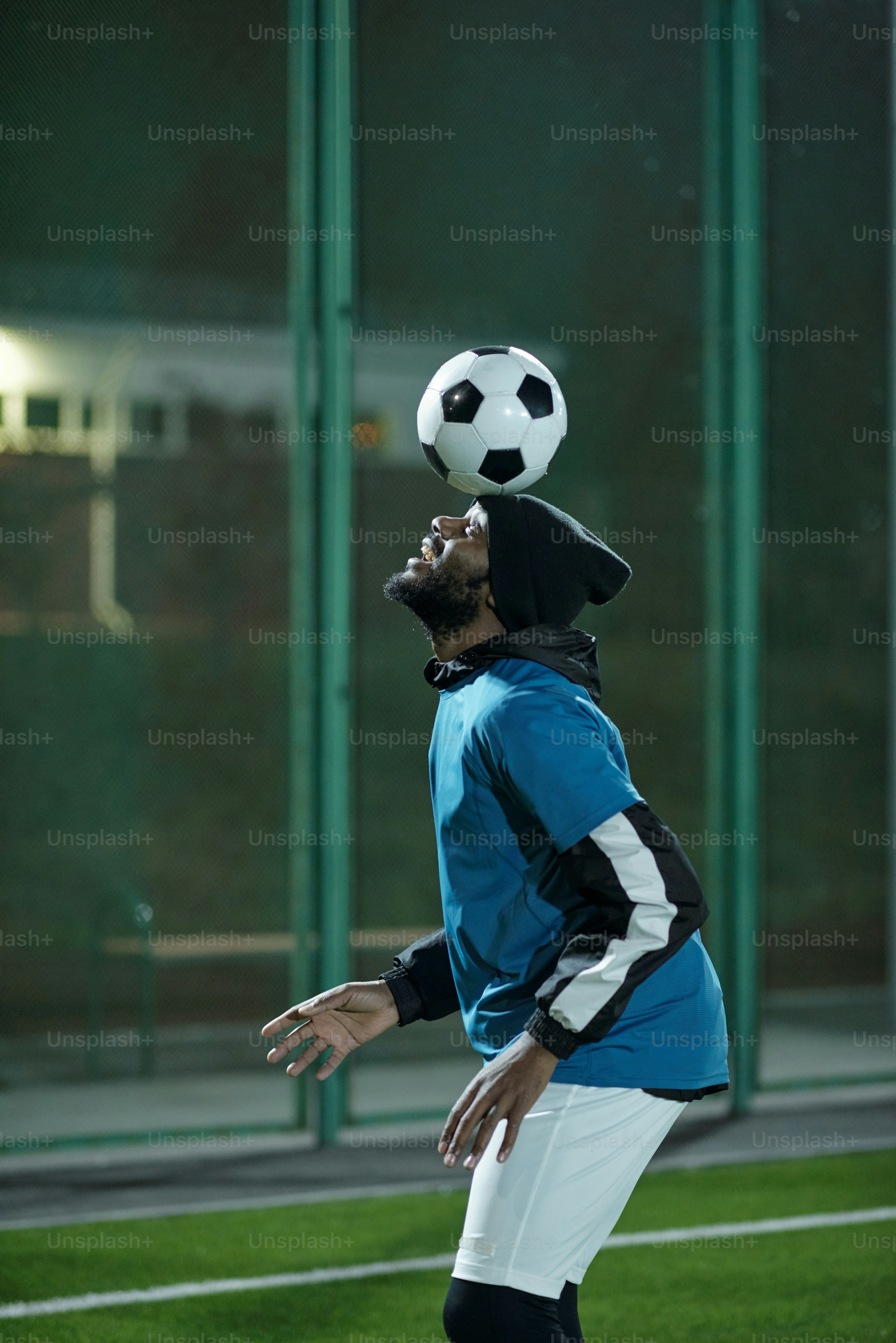 Junger gutaussehender Mann in Sportuniform, der beim Training im Stadion mit Fußball auf der Stirn trainiert