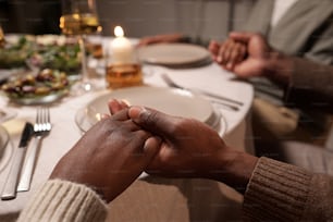 Hands of young African couple sitting by festive table served with homemade food and praying before eating