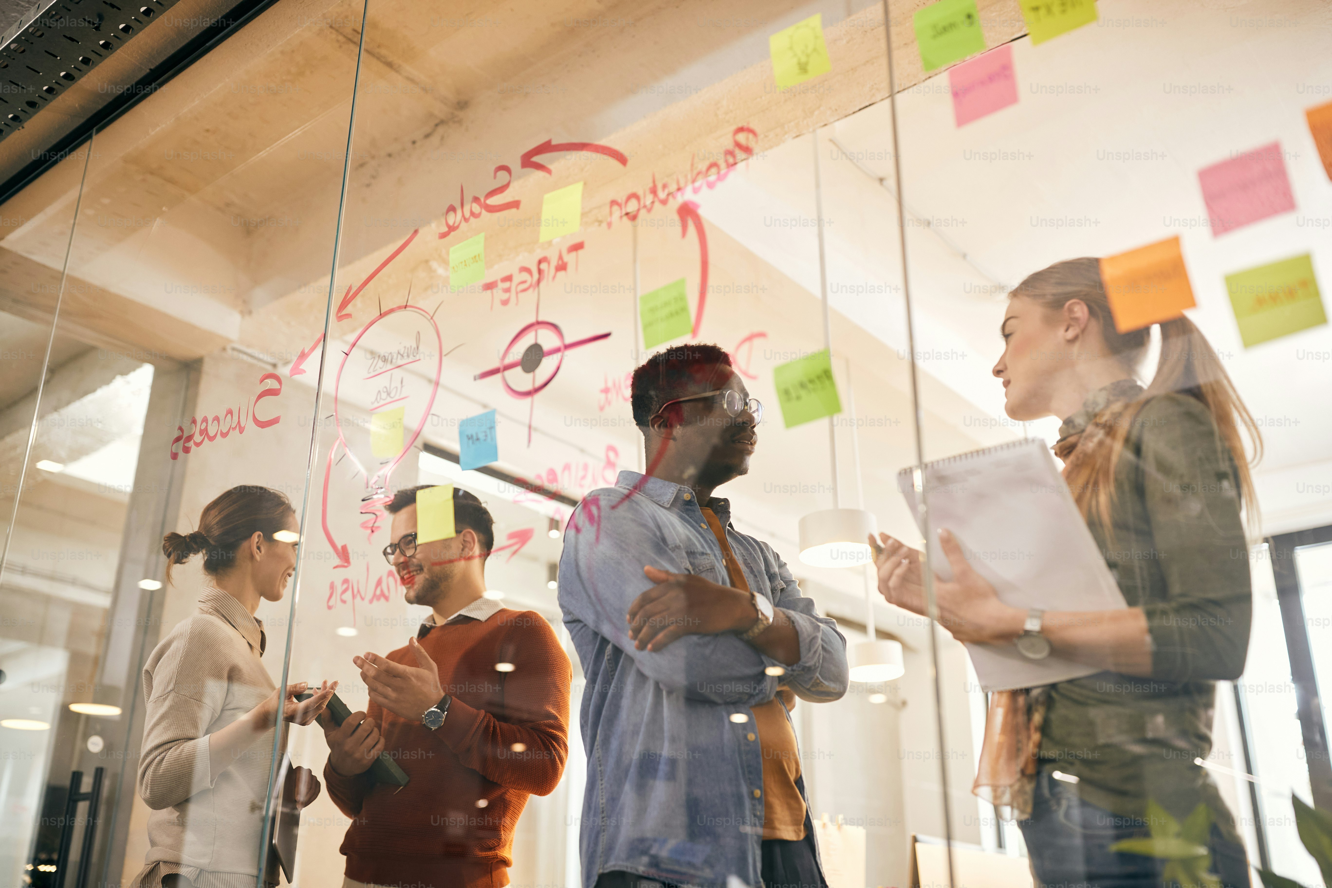 Low angle view of multi-ethnic team of business colleagues communicating while analyzing plans on glass wall in the office.