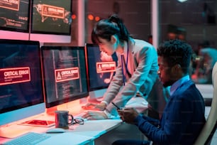 Dois jovens programadores interculturais tentando resolver problema técnico na frente de computadores com erro crítico nas telas