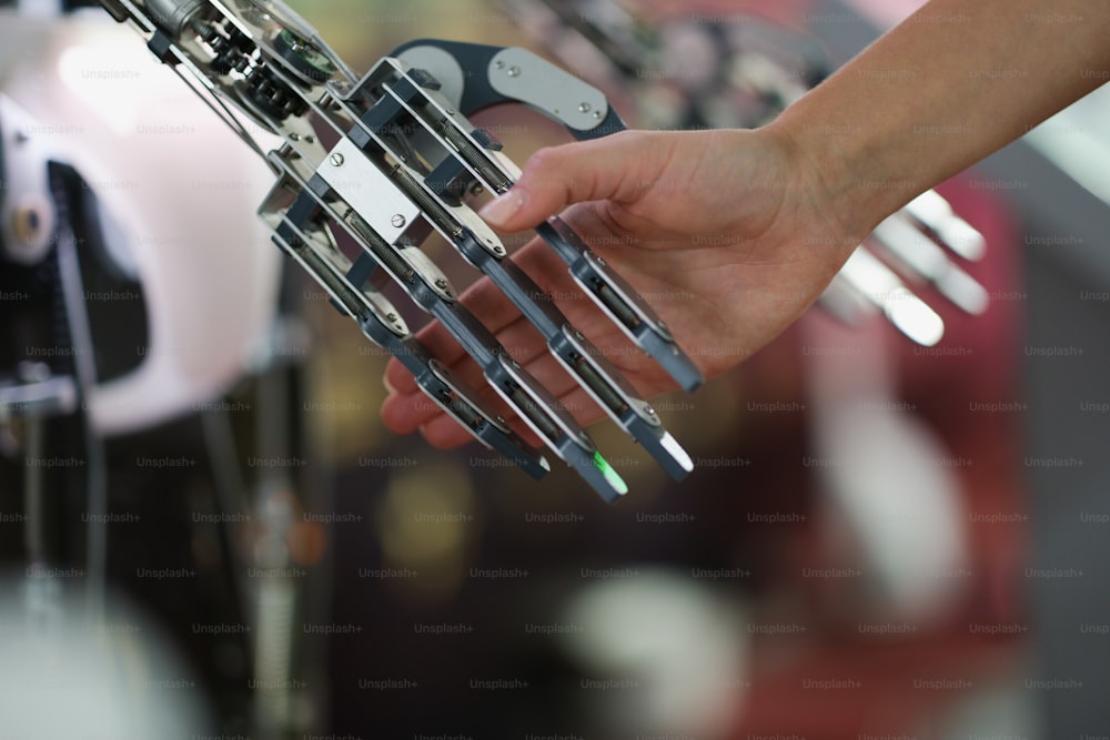 Uma mão feminina segura a mão de metal de um ciborgue, close-up. Estrutura de robô de aço, automação de processos, equipamentos futuristas