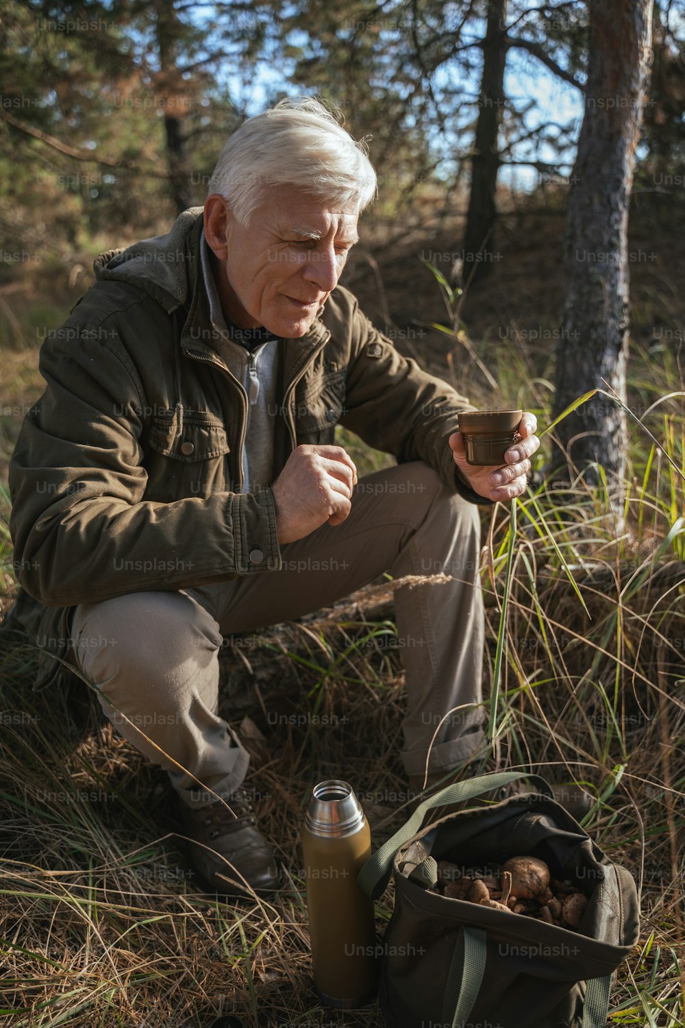 Vertikale Aufnahme des älteren männlichen Reisenden, der nach dem Wandern und Pilzsammeln ein Getränk trinkt. Hobbys und Erntekonzept