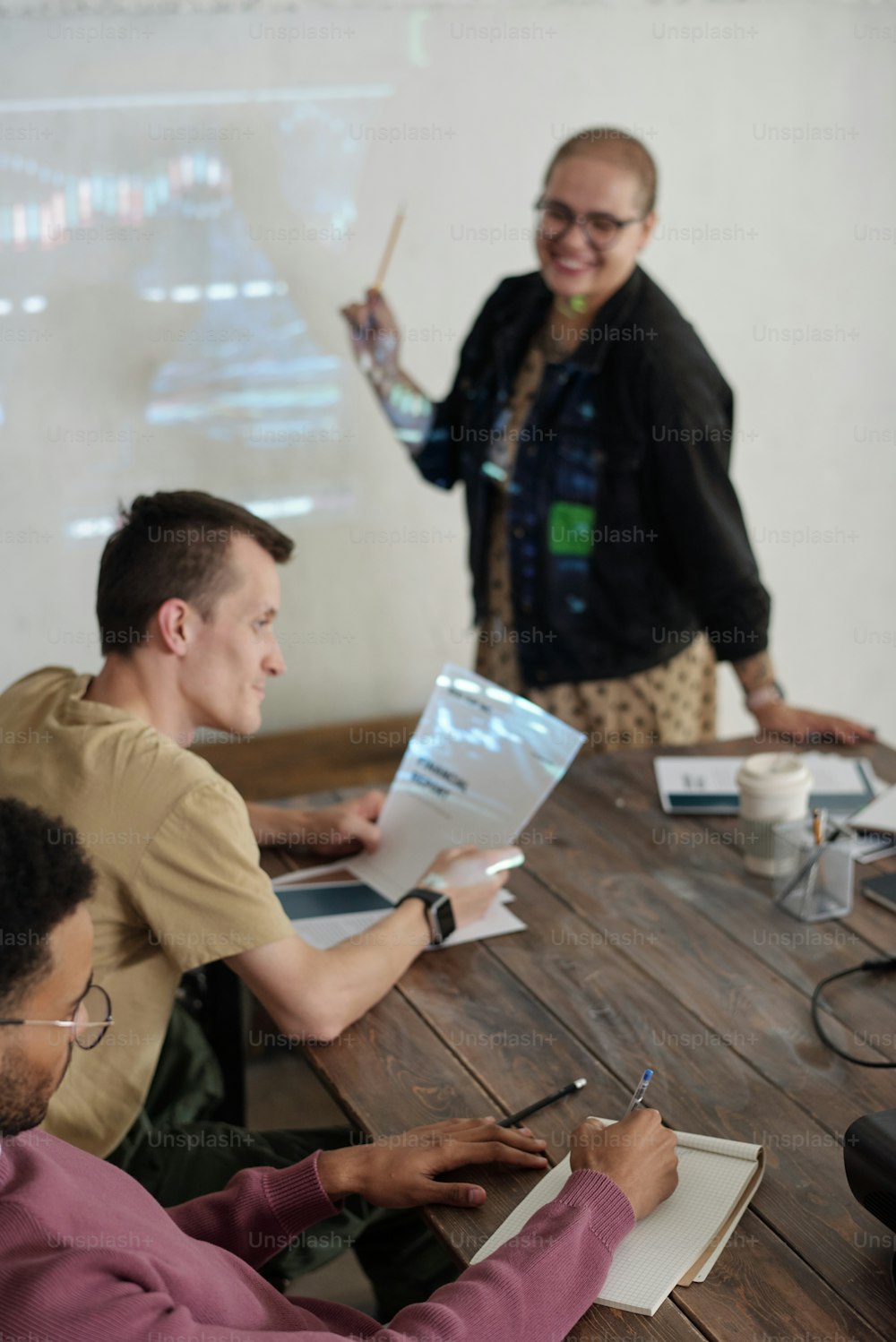 Uno de los jóvenes compañeros de trabajo tomando notas en el bloc de notas mientras escuchaba al entrenador y a sus colegas discutir los datos financieros en el seminario