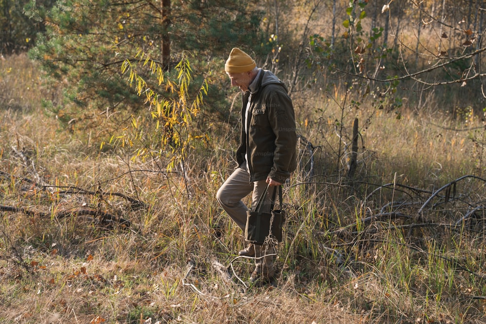 Ganzkörperansicht des älteren Mannes, der während des sonnigen Herbsttages durch den Wald geht und Pilze sammelt. Archivfoto