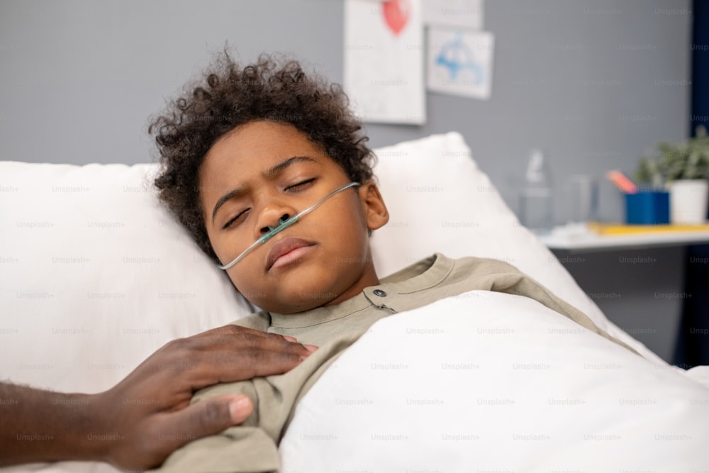 病棟のベッドで意識不明に横たわっている鼻にチューブを入れたアフリカの小さな男の子