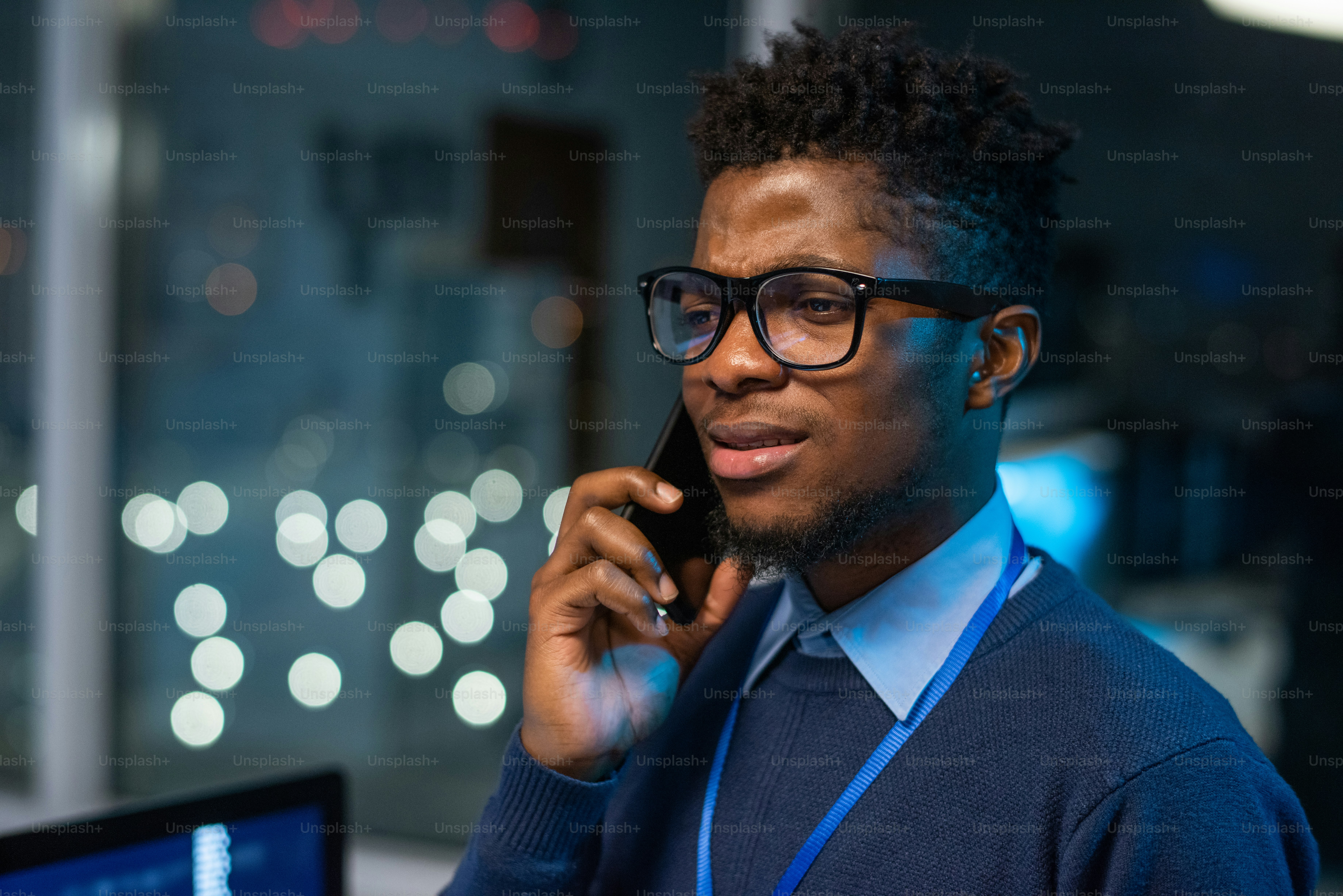 眼鏡をかけた若いビジネスマンがオフィス環境を背景にカメラの前でスマートフォンで話す