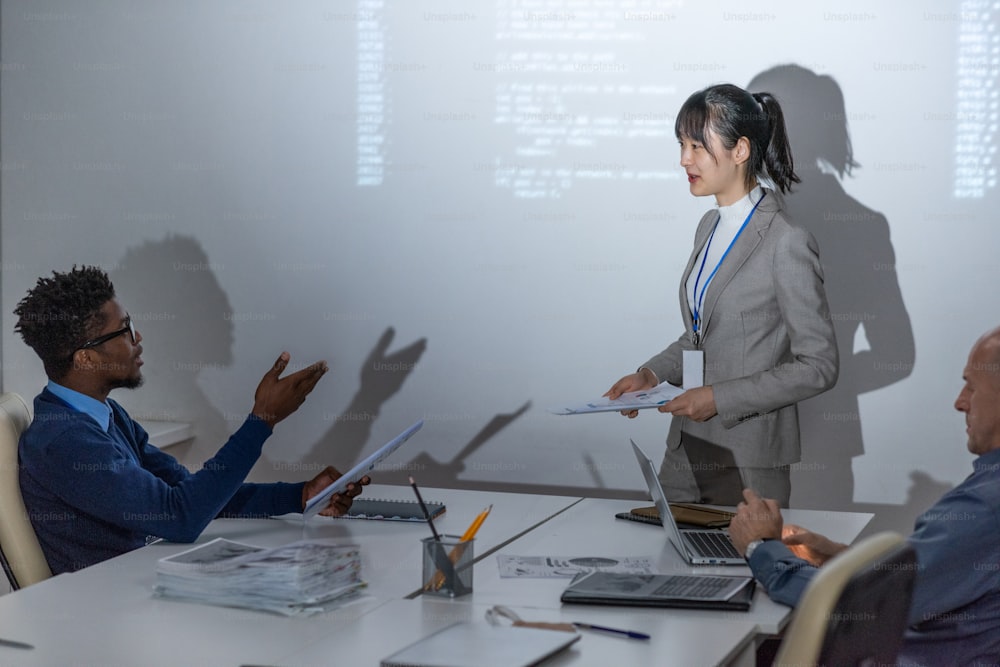 Young African businessman talking to Asian female colleague standing by large interactive whiteboard