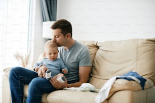 Young loving father enjoying in time with his baby son and kissing him at home. Copy space.