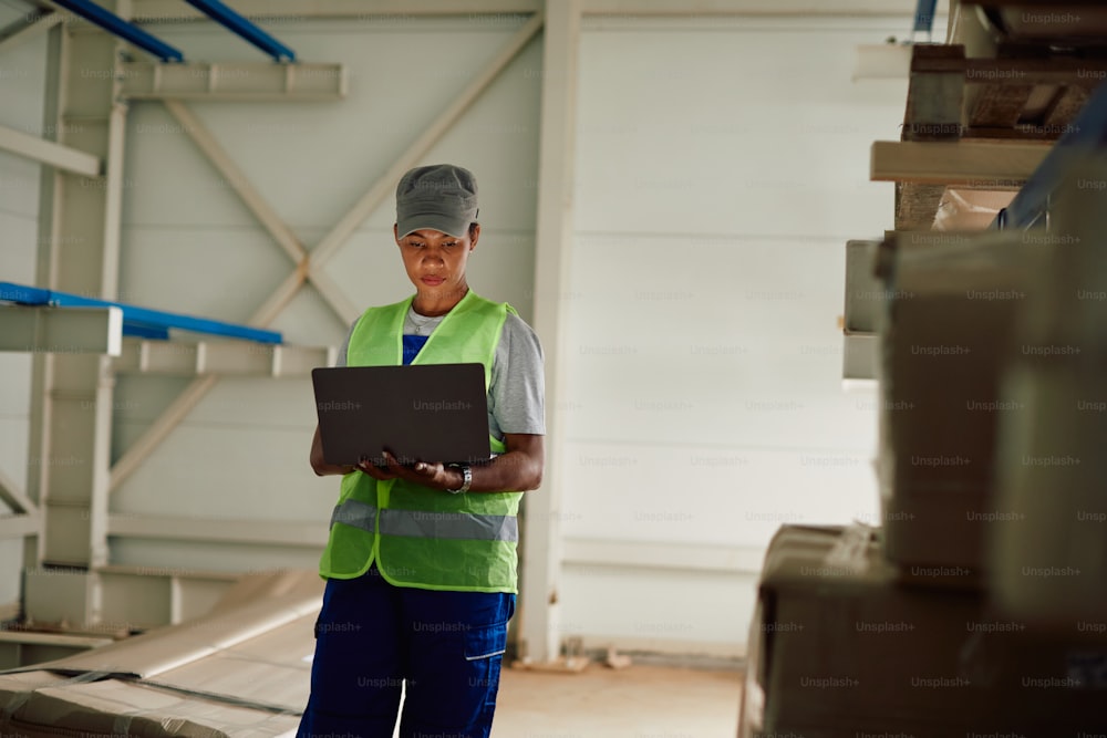 African American woman working on laptop at distribution warehouse.